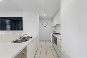 Una cocina compacta con un lavamanos de acero inoxidable, un reloj en la pared y una estufa a gas.