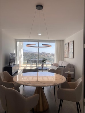 Un comedor moderno con una amplia mesa de mármol, rodeada de sillas, y vistas a un balcón con mobiliario exterior.