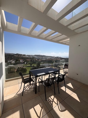 A balcony with a table and chairs, a clear view of a cityscape, and a tiled floor. - AS EXT Cala Casa Banderas (Mijas)
