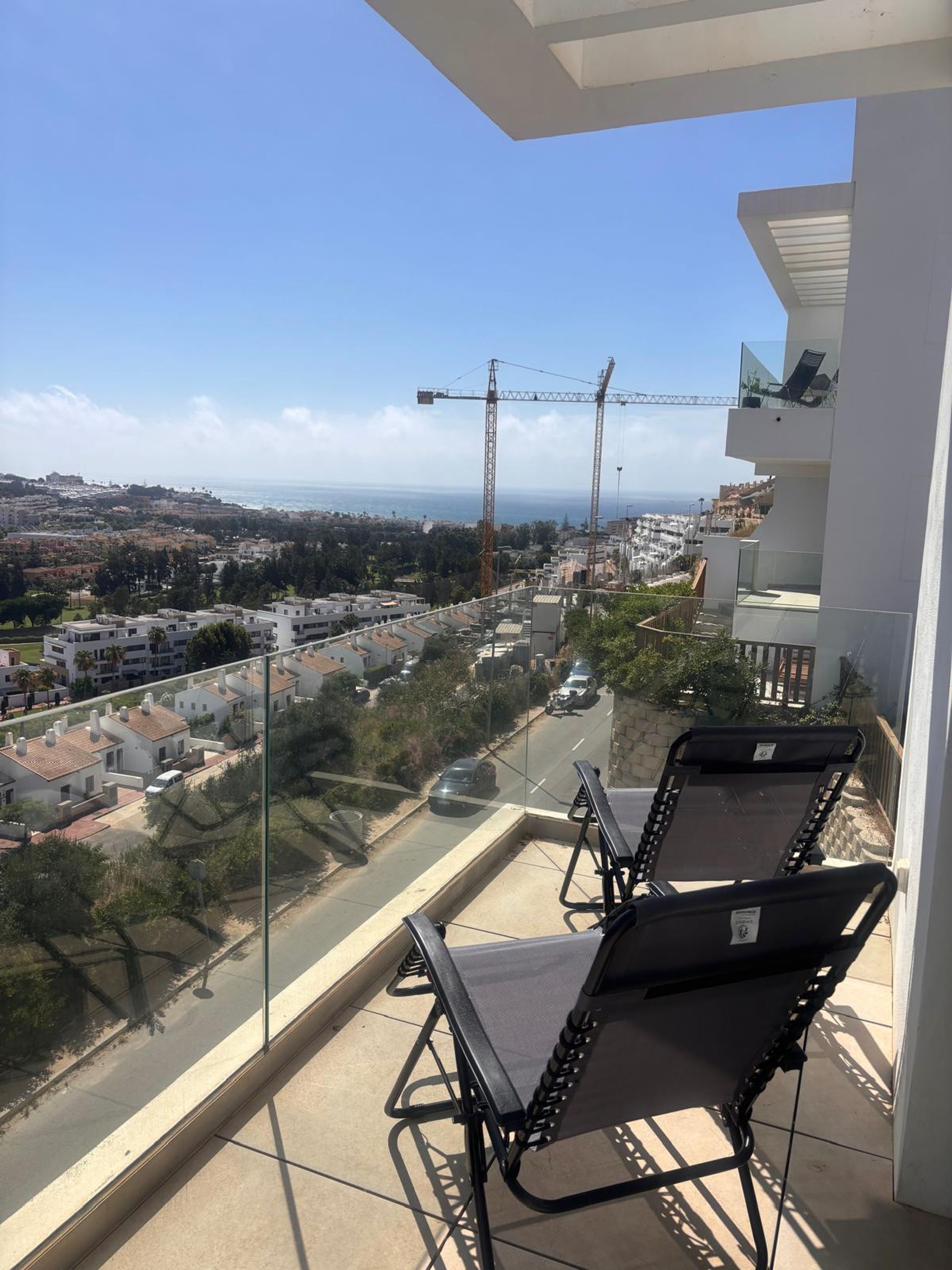 A balcony with a view of a construction site, a crane, and a residential area.
