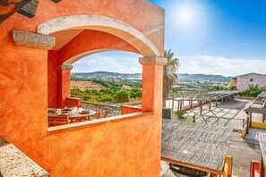 A terrace with a table and chairs, a view of the countryside, and a building with an orange facade. - TORO I (Apartment for 4 Guests - 30' from Porto Cervo) (Santa Teresa Gallura)