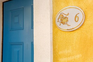 A door with a number '6' and a lion emblem on a textured yellow wall. - Leone Flat VI (30' from Porto Cervo) + Private Terrace (Santa Teresa Gallura)
