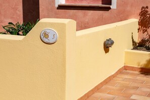 Eine gelbe Wand mit einer Hausnummer und einem Wasserhahn.