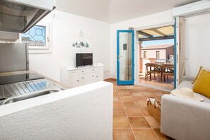Eine kompakte Küche mit eingebautem Herd, einer weißen Arbeitsplatte und einem Fernseher. Eine Glastür führt auf eine Terrasse mit Tisch und Stühlen.