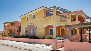 A two-story building with a yellow facade, arched windows, and a gated entrance. - TORO III (Apartment for 4 Guests - 30' from Porto Cervo) (Santa Teresa Gallura)