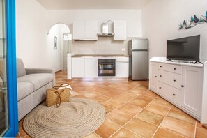 Eine kompakte Küche mit weißen Schränken, einem Einbauofen, einem Kühlschrank und einem Flachbildfernseher auf einem weißen Schrank.