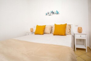 A bed with a white headboard, two yellow pillows, a beige bedspread, and a small white nightstand with a wicker basket. - Bilancia IV (Apartment - 6 guests - Free parking)   (Santa Teresa Gallura)