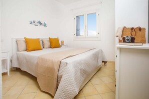 Ein Schlafzimmer mit einem Bett, einem Fenster, einem Regal mit Kamera und Tasche, sowie einer Wanddekoration.