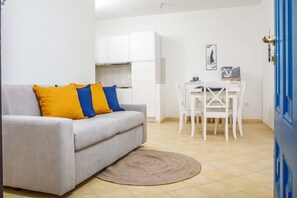 Ein gemütlicher Wohnbereich mit einer Couch, einem Esstisch mit Stühlen, einer Küchenzeile und einer blauen Tür.
