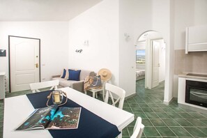 Ein Zimmer mit Esstisch, Stühlen, einer Sitzecke und einer Küchenzeile, mit Blick durch einen Bogen.