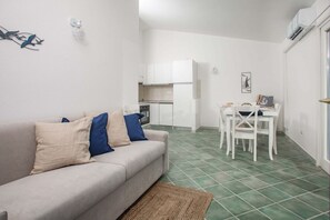 A compact living space with a sofa, dining table, chairs, kitchenette, and a small rug. - Bilancia VI (Sea View Apartment - 30' from Porto Cervo) (Santa Teresa Gallura)