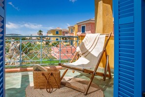 A balcony with a chair, a wicker basket, and a view of colorful buildings. - Bilancia VI (Sea View Apartment - 30' from Porto Cervo) (Santa Teresa Gallura)