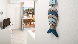 Habitació amb televisió sobre un prestatge, un peix decoratiu penjat a la paret i vista a un pati exterior amb mobles.