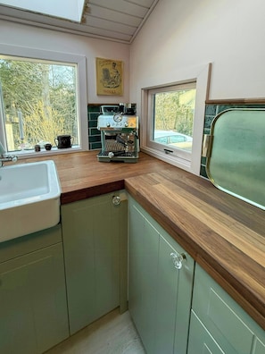 Eine kleine Küche mit einer Holzausziehtafel, einer Kaffeemaschine und einem Fenster mit Blick auf Bäume.