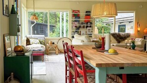 A spacious dining area with a wooden table, red chairs, and a hanging light fixture. - Colourful summer house on Bornholm (Hasle)