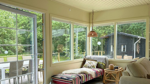 A cozy room with a bed, a chair, a table, and large windows. - Colourful summer house on Bornholm (Hasle)