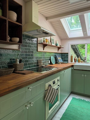 Una cocina con gabinetes verdes, encimera de madera, tragaluz y vistas al exterior.