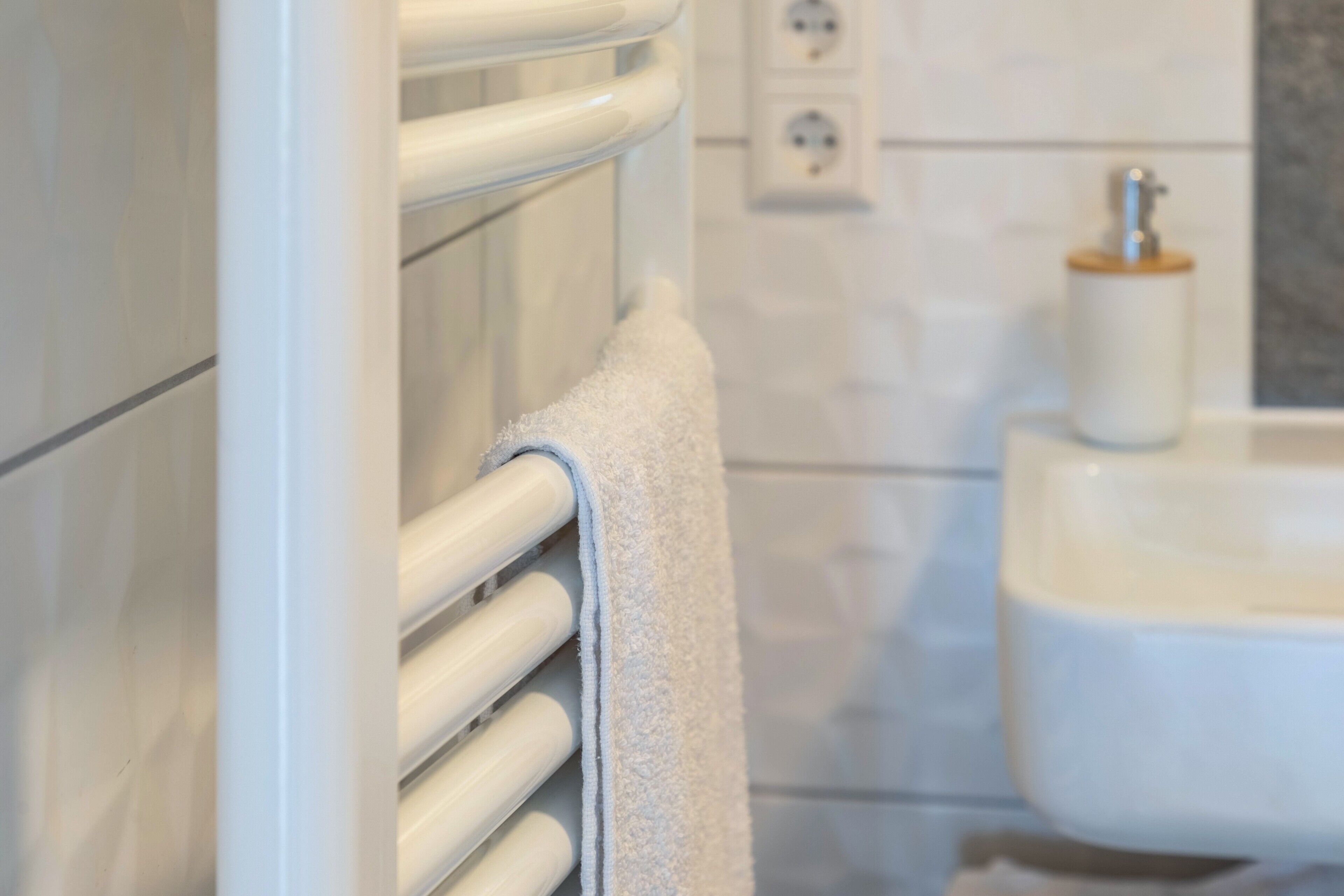 Une salle de bain avec une serviette blanche suspendue à un radiateur, un lavabo blanc et une prise électrique au mur.