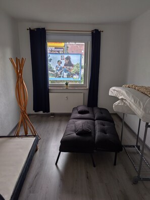 Um quarto com cama, um banco, uma janela com cortinas e um radiador.