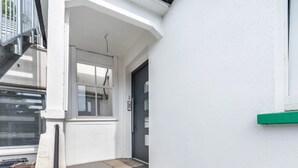 A white exterior with a grey door, a window, and a small set of stairs leading to a door. - Cozy Apartment in the Heart of Heidenheim an der Brenz (Heidenheim)