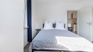 A single bed with a patterned bedspread, a bedside table, a small round table, and a window with curtains. - Cozy Apartment in the Heart of Heidenheim an der Brenz (Heidenheim)