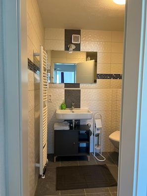 Uma casa de banho compacta com uma sanita, uma pia branca, um espelho em cima e um porta-toalhas.
