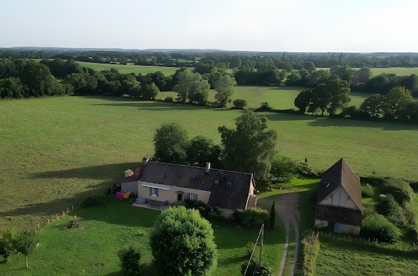Une propriété rurale comprenant une maison principale et une dépendance plus petite, le tout entouré de vastes champs verdoyants et d’arbres.