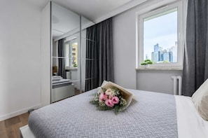 A modern bedroom with a large bed, a window with a city view, a mirror, and a small plant on the windowsill. - Lumina 3-rooms Apart near the Główna Train Station I Balcony (Warszawa)