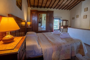 Ein Hotelzimmer mit einem Bett, einem Nachttisch aus Holz mit einer Lampe, einem Holzschrank und einer Tür, die auf einen Balkon führt.