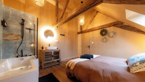 Ein Schlafzimmer mit einem großen Bett, einer Holzbalkendecke, einem Badezimmer mit Badewanne und einem Spiegel.