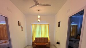A spacious living area with a sofa, a coffee table, a ceiling fan, and a window with curtains.