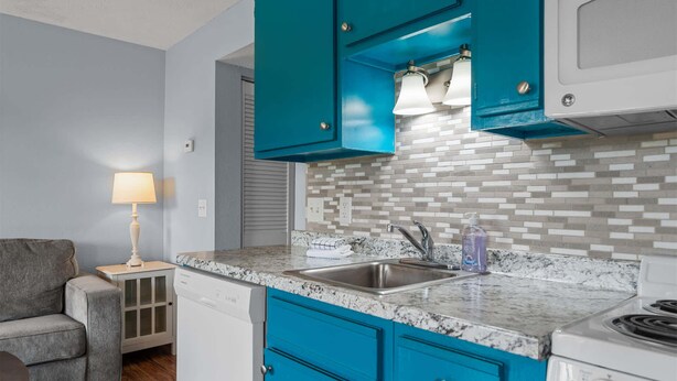 A compact kitchen with teal cabinets, a granite countertop, a built-in stove, and a sink. - Scenic Cottage at Fall Creek (Branson)