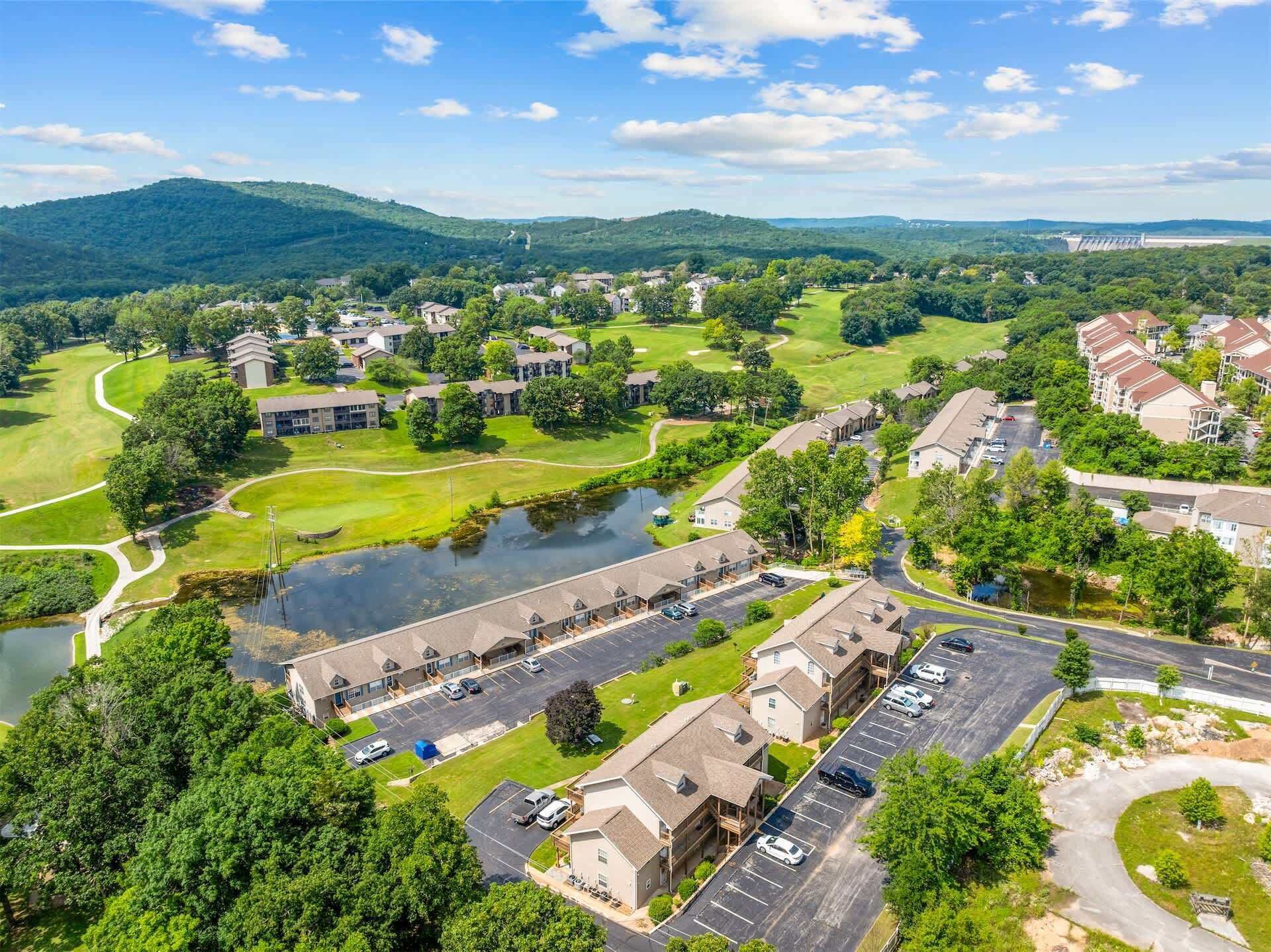 A residential area with a golf course, a large building with a parking lot, and a body of water.