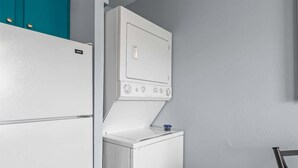 A compact laundry room with a white washing machine and dryer, teal cabinets, and a metal ladder. - Scenic Cottage at Fall Creek (Branson)