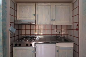 Una cocina compacta con estufa, horno y lavabo, armarios de madera y salpicadero de azulejos.