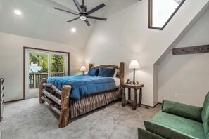 Un dormitorio con cama, mesita de noche, lámpara, ventilador de techo, ventana y vistas al exterior.