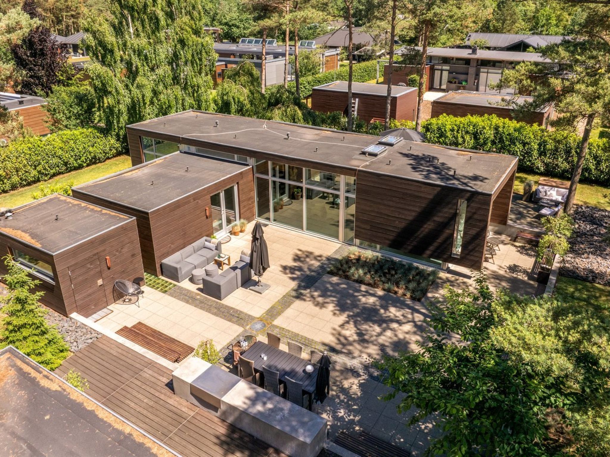 A modern house with a flat roof, large glass windows, and a patio area with outdoor furniture.
