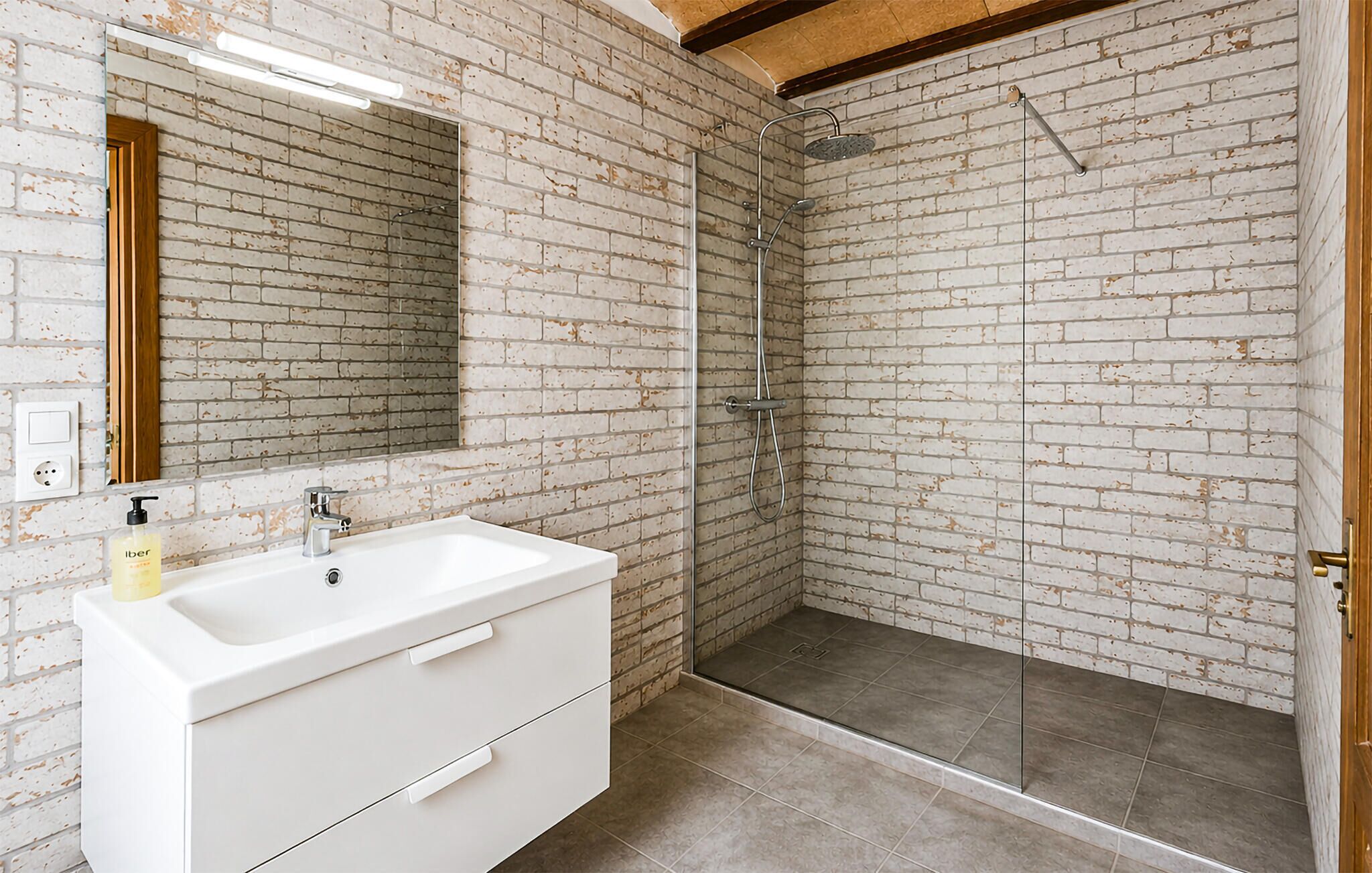 A bathroom with a white sink, mirror, and shower with a brick wall backdrop.