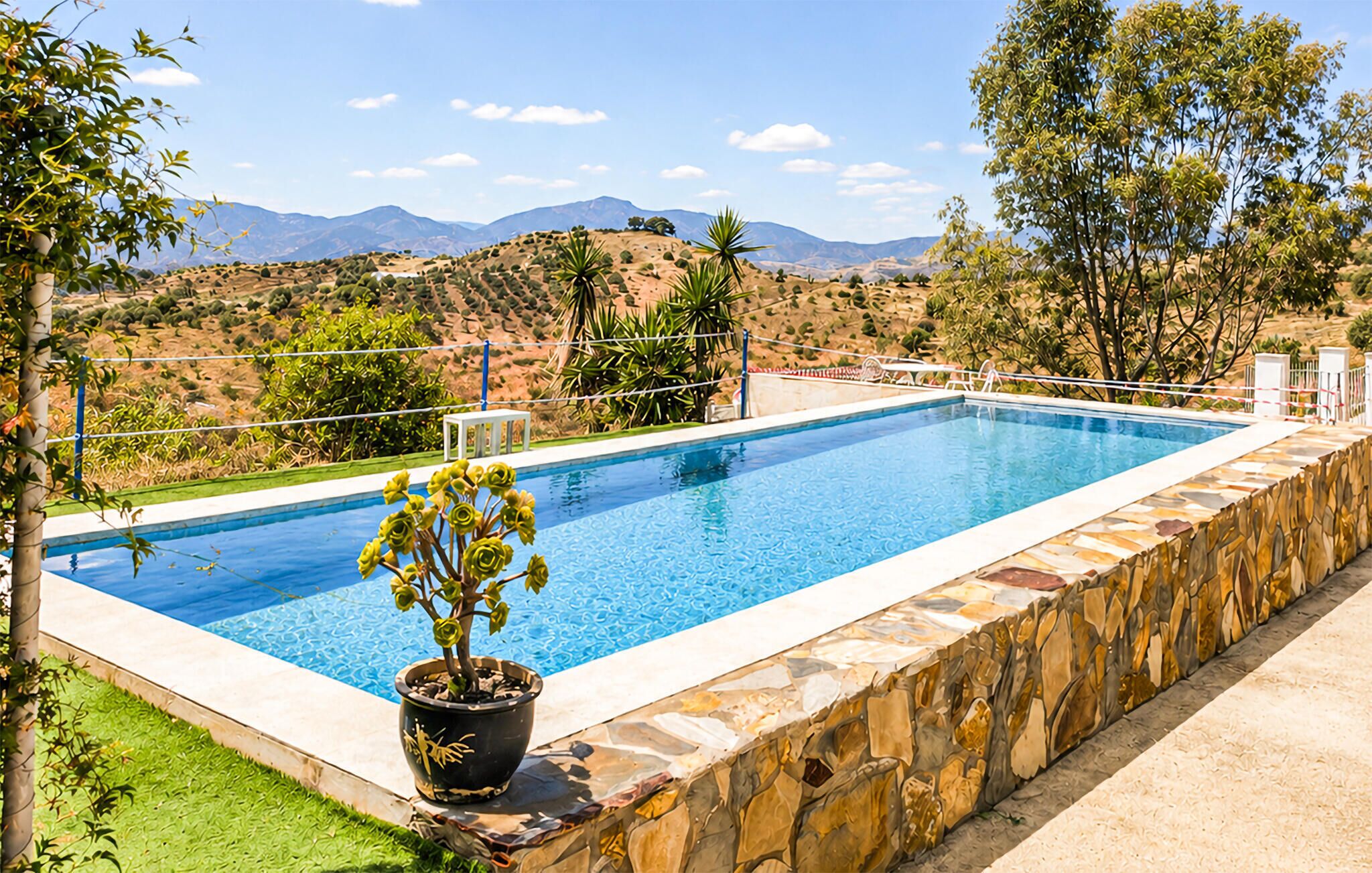 Une piscine rectangulaire bordée de pierres, entourée d’une pelouse et offrant une vue sur des collines lointaines.