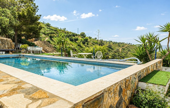 A rectangular swimming pool with stone edging, surrounded by a patio with outdoor furniture, a grassy area, and a hilly landscape in the background. - Gorgeous home in Pizarra with private swimming pool, can be inside or outside (Pizarra)
