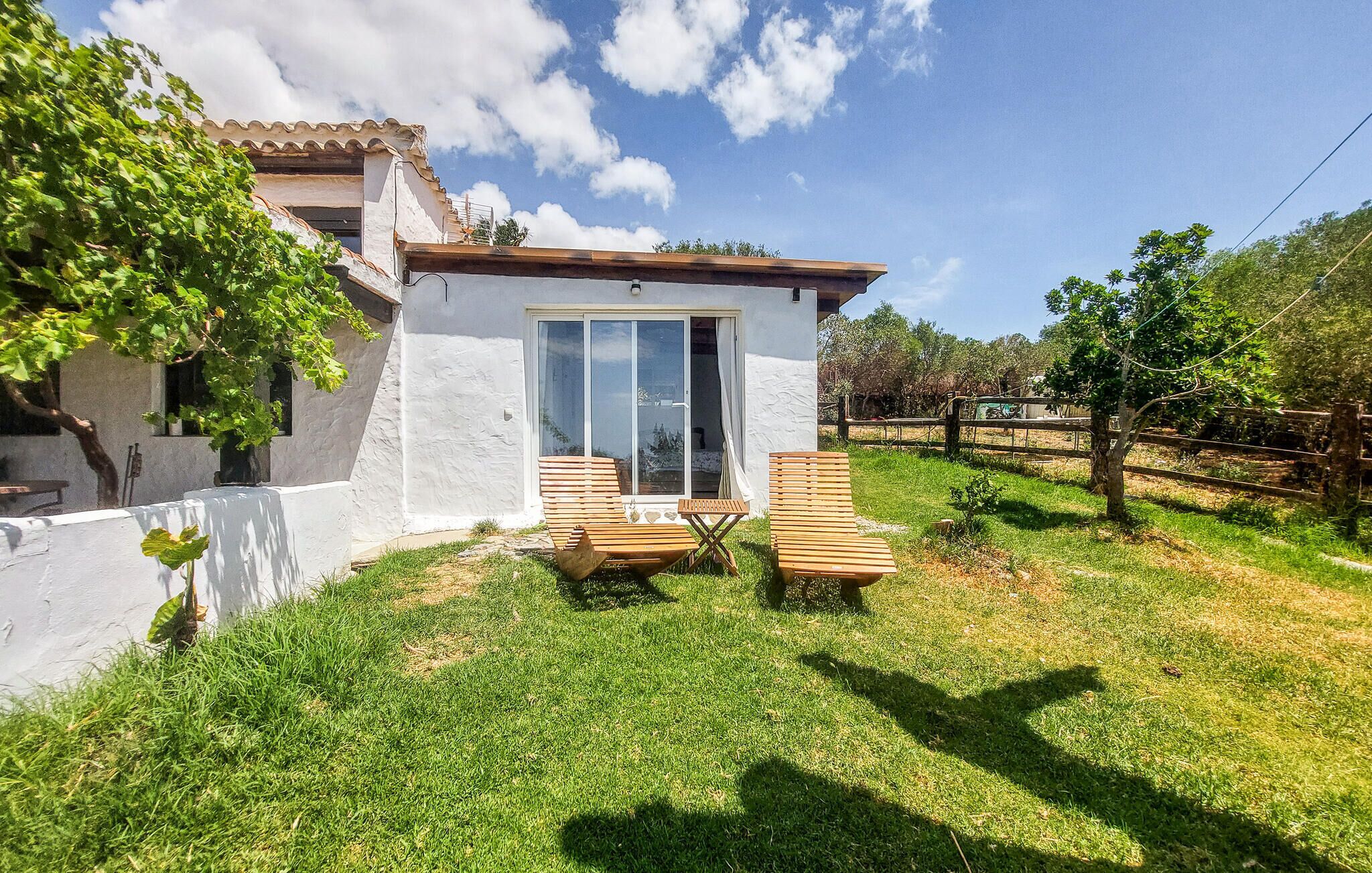A small white building with a glass door, two wooden chairs, and a table in the yard.