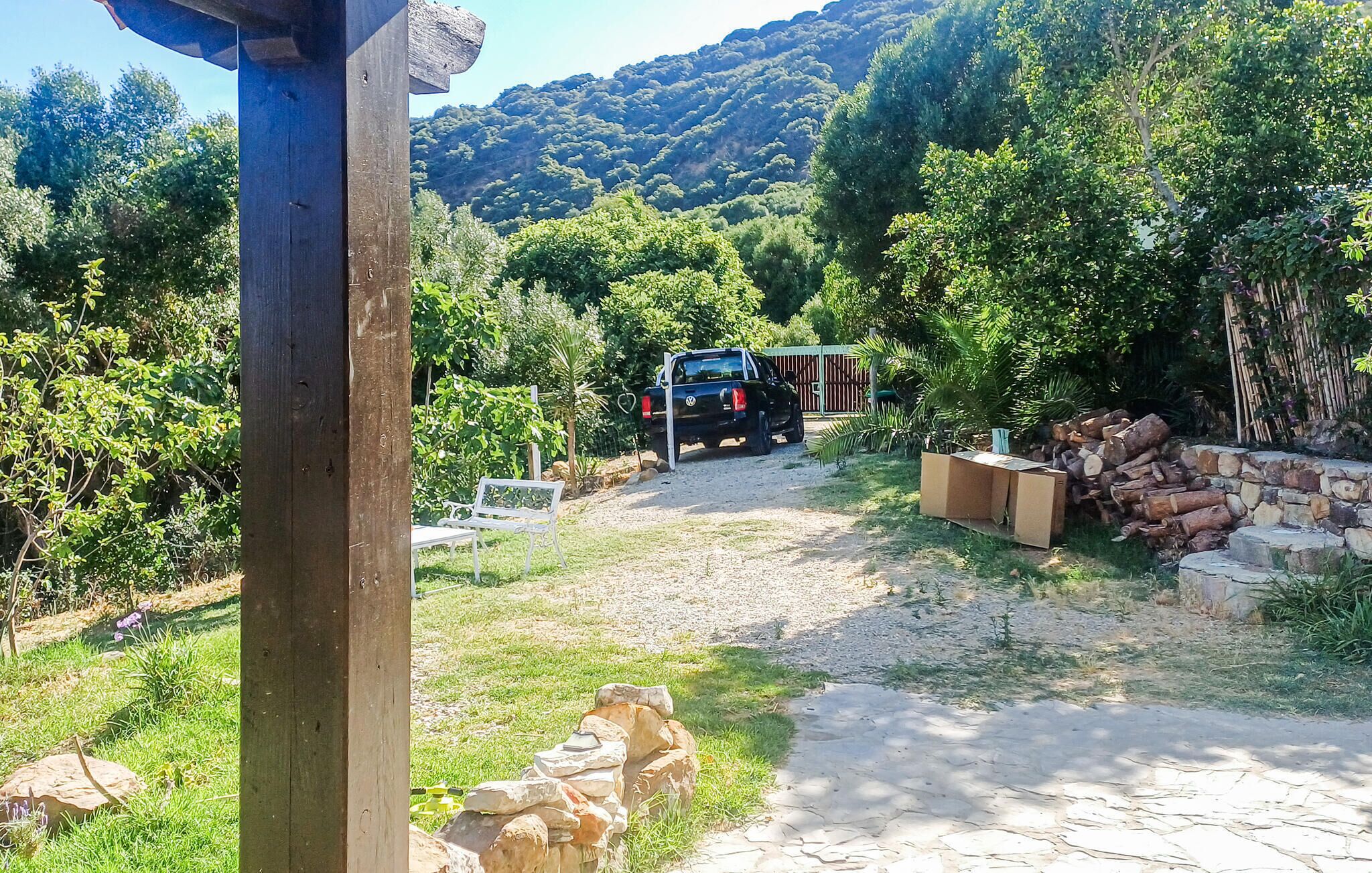 A vehicle parked in a rural setting with a stone wall, a wooden structure, and a path leading to a gate.