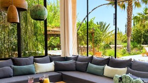 Un saló modern amb un sofà modular, una taula de centre rodona de fusta i un gran finestral que ofereix vistes a vegetació i una pérgola.