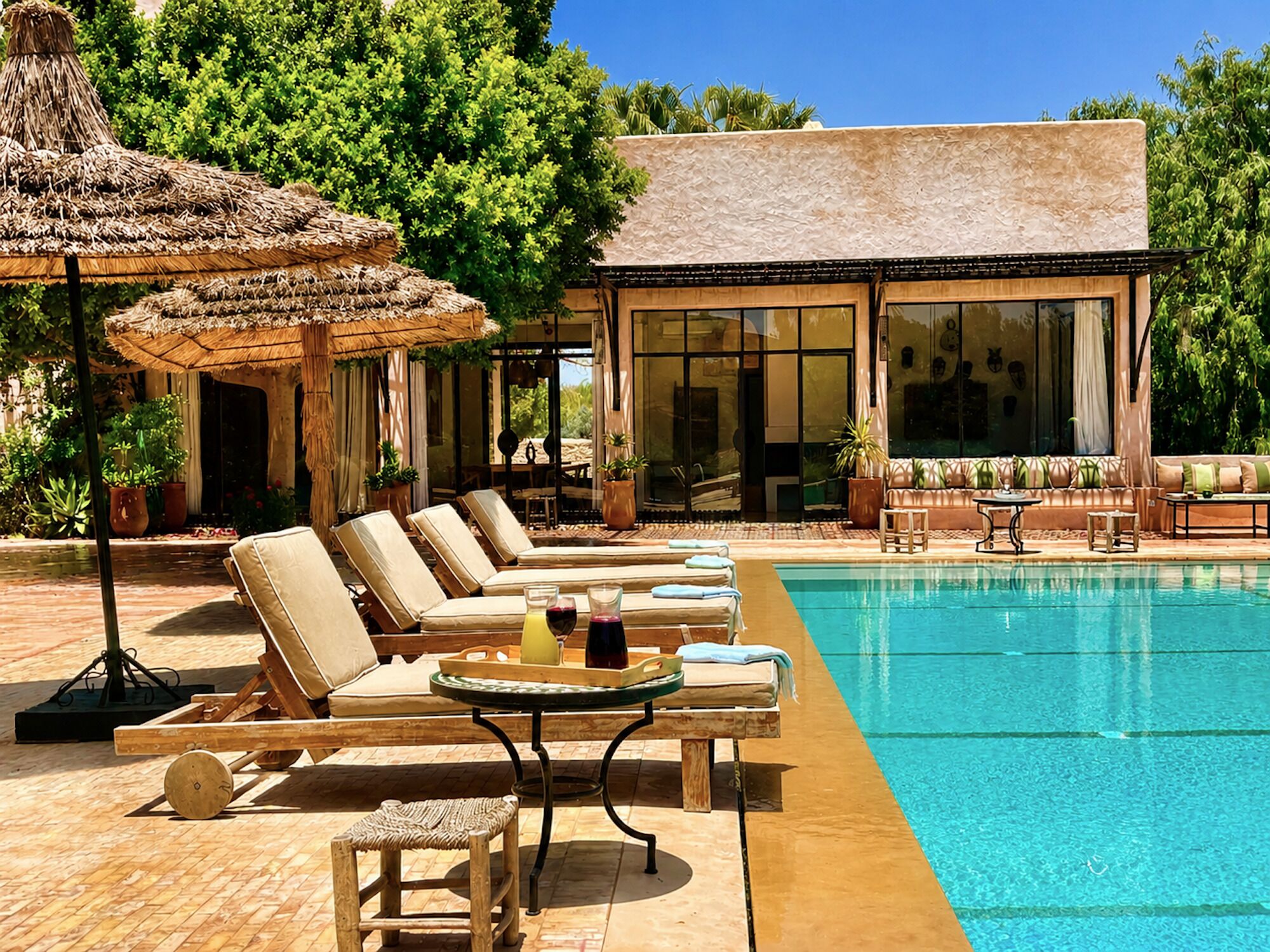 A poolside area with lounge chairs, a table with drinks, and a building with large windows.