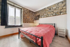 A bedroom with a stone wall, a window with curtains, a bed with a metal frame, and a white dresser. - Apartment 'Centre Crozon' with Wi-Fi (Crozon)