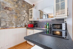 Eine Küche mit einer Steinwand, einer schwarzen Arbeitsplatte, einem roten Toaster, einer Mikrowelle und einem Schrank mit Glastüren.