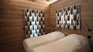 Ett sovrum i en stuga med träpanel, två sängar, träväggar och ett sluttande tak.