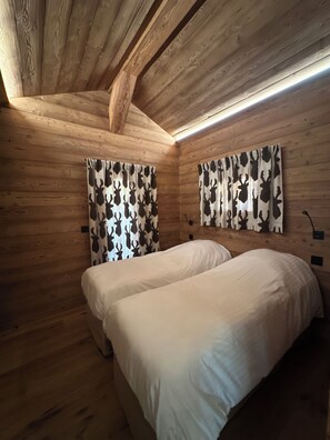 Ein Schlafzimmer einer Holzhütte mit zwei Betten, Holzwänden und einer geneigten Decke.