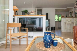 A modern living room with a wooden chair, a coffee table with a woven placemat, and a blue pitcher with white polka dots. - Retro home with three terraces near the beach (Glesborg)