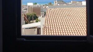 A view through a window of a building with a tiled roof, a clear sky, and a distant coastline. - TUAREG Hotel (Maruggio)